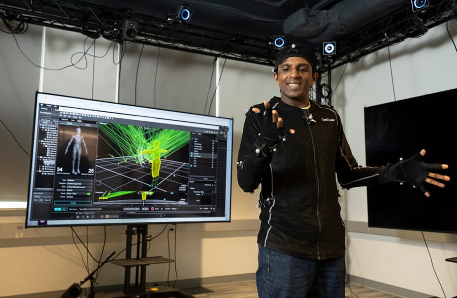 A person wearing a motion capture suit stands in front of a screen displaying motion capture data.