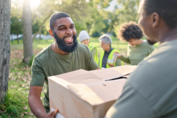 A man with a beard is handing a box to another man in a group of people.