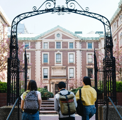 A group of students walk past an iron gate in front of a building.