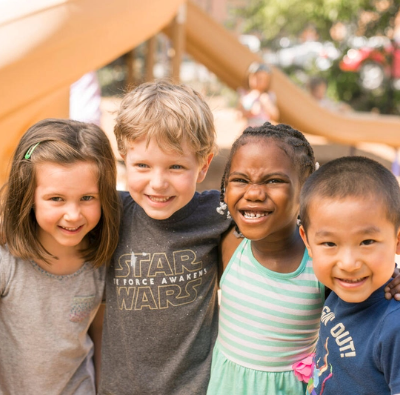 A group of children smiling in front of a playground.