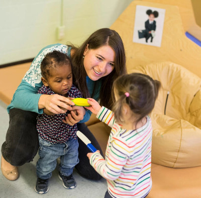 A woman is playing with two small children in a playroom.