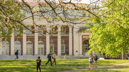 A group of people walking on the grass in front of a building.