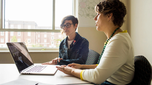 Two women sitting at a table with a laptop in front of them.