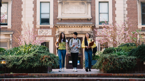 Three students walking down the steps of a brick building.