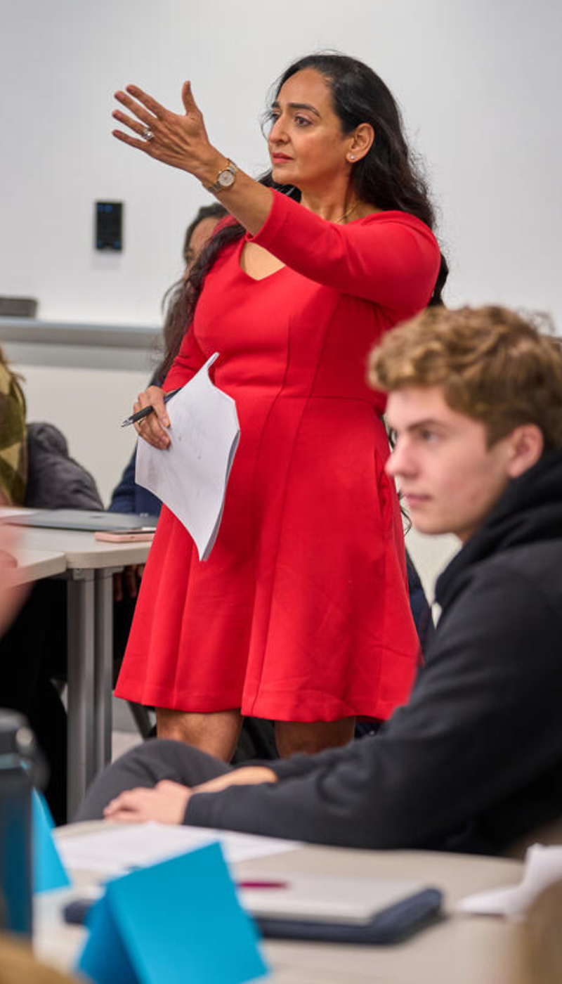 A woman in a red dress is giving a lecture to a group of students.