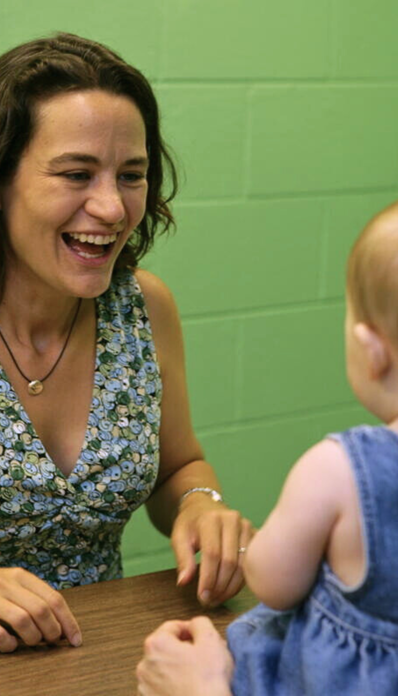 A woman laughing with a baby at a table.