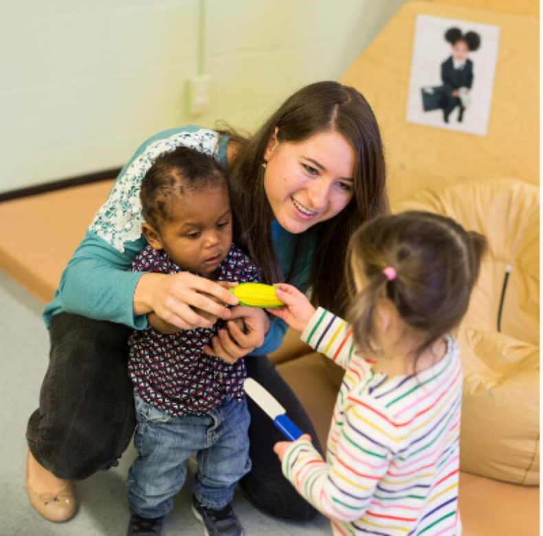 A woman is playing with two children in a playroom.