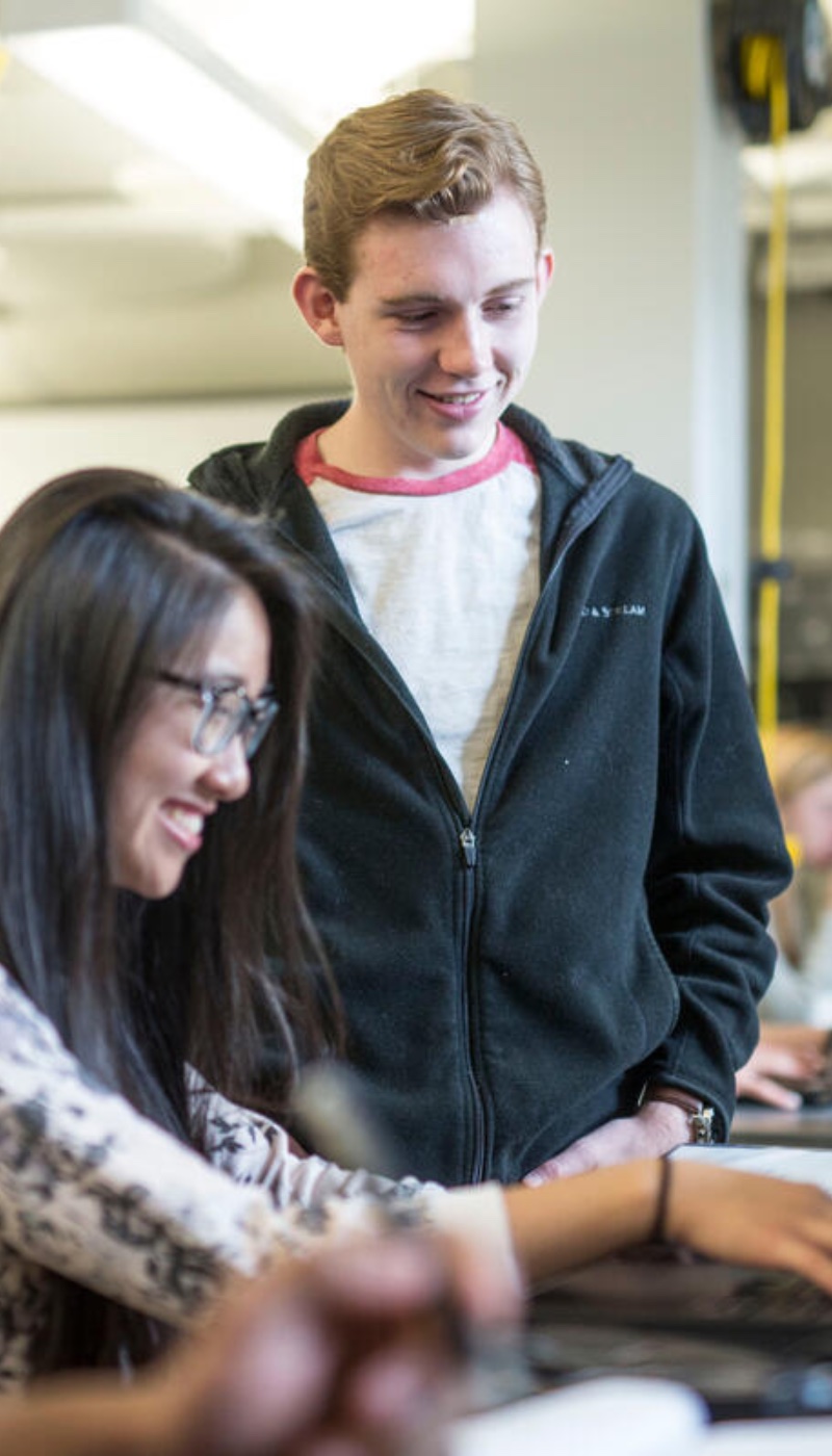 Two students working on a laptop in a classroom.