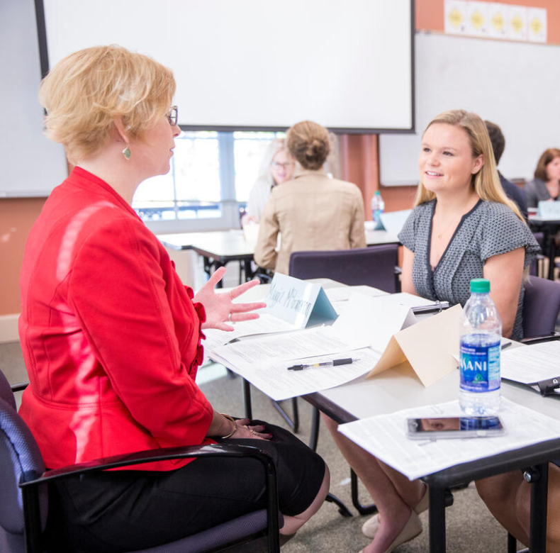 A group of women talking at a table in a classroom.