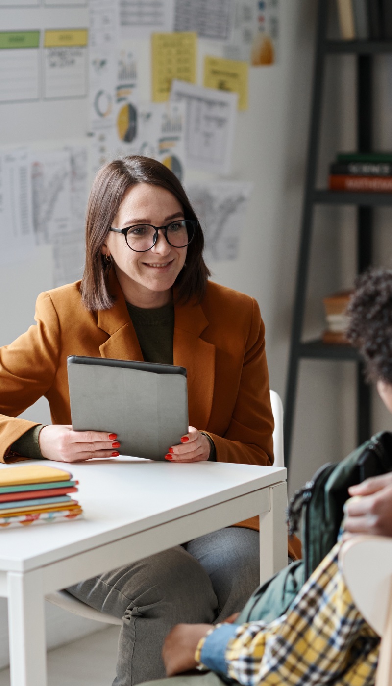 A woman talking to a student with a tablet in front of her.