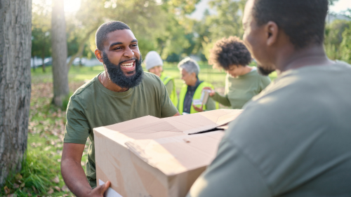 A man with a beard is handing a box to another man in a group of people.