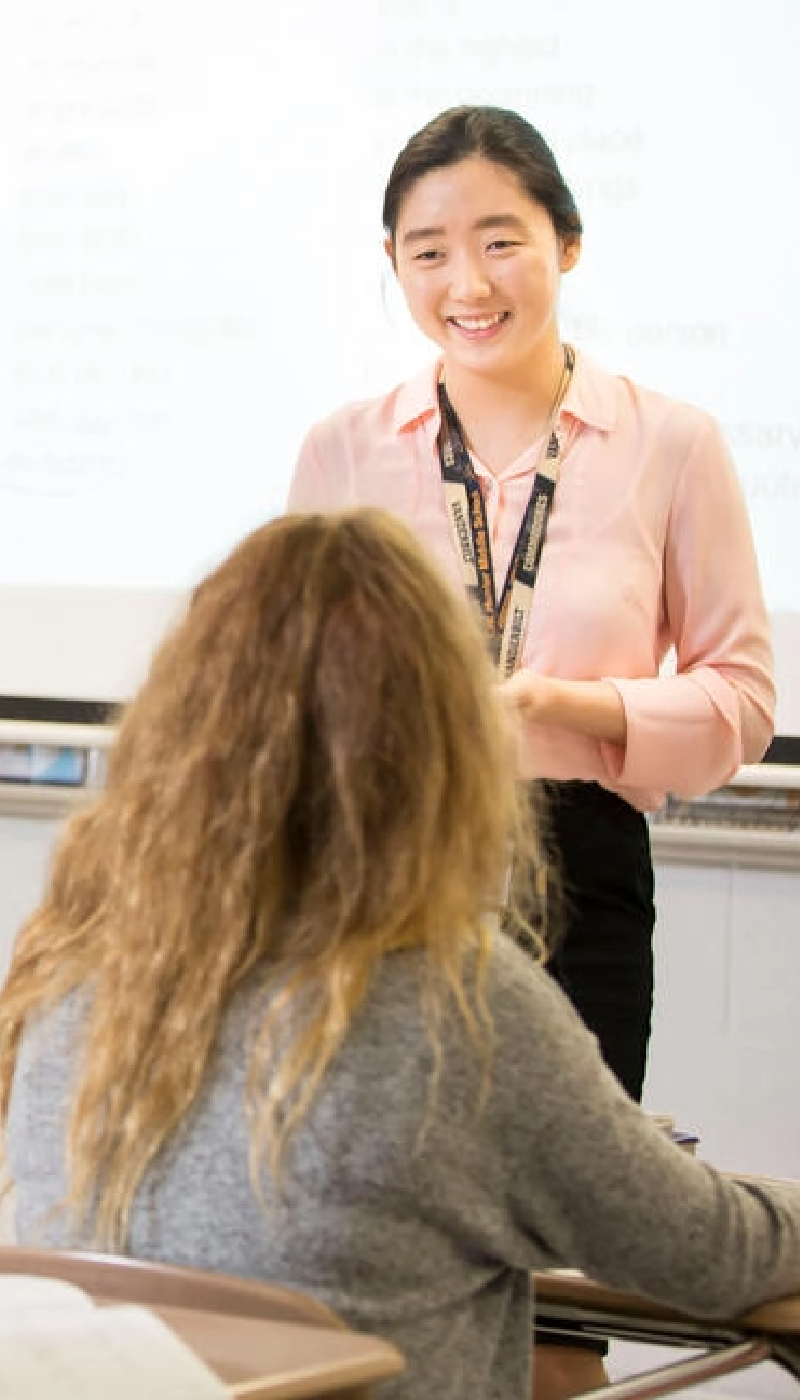 A woman in a pink shirt is talking to a student in a classroom.