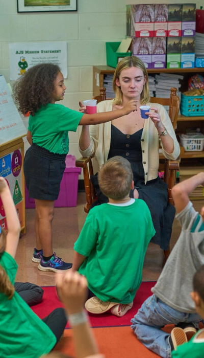 A woman in a green shirt is teaching children in a classroom.