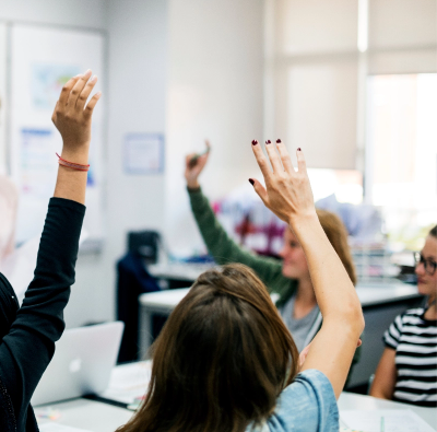 A group of people raising their hands in a classroom.